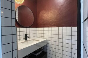 A bathroom with a white sink, black faucet, and a round mirror on the wall. - Fangwu Youth Hostel (Guiyang)