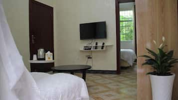 Una habitación con una cama, un televisor en la pared, una mesita pequeña y una planta en maceta.