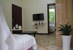 A room with a bed, a TV mounted on the wall, a small table, and a potted plant. - Fangwu Youth Hostel (Guiyang)