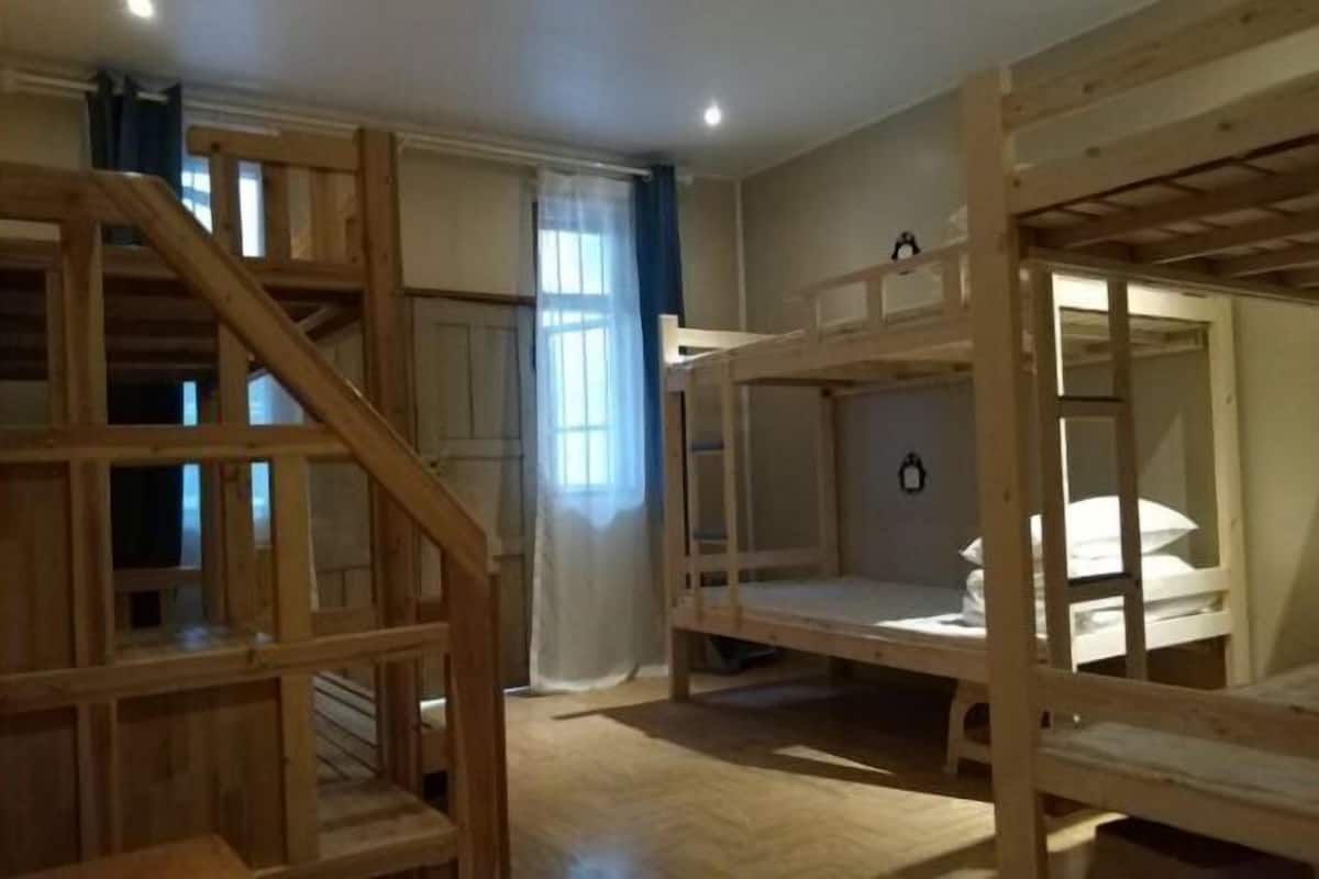 A room with bunk beds, a wooden staircase, and a window with curtains.