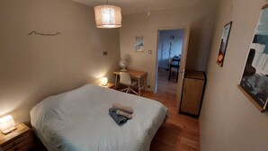 Una camera da letto con un letto grande, una scrivania e una sedia. Si nota un tavolino con una lampada e un quadro appeso al muro.