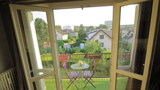 Una stanza con un'ampia porta vetrata che dà su un balcone con tavolo e sedie.