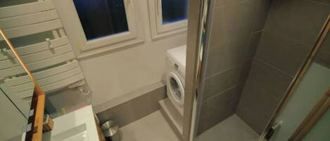 Une petite salle de bain comprenant une douche, des toilettes et un lave-linge.