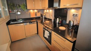 Una cucina moderna con mobili in legno, un piano di lavoro nero, elettrodomestici in acciaio inossidabile e un piccolo angolo ristoro.