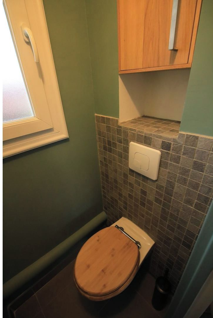 A bathroom with a wooden toilet, a tiled wall, a window, and a wooden cabinet.