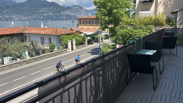 Un balcon donnant sur une route côtière, un bâtiment avec un toit recouvert de tuiles rouges et une montagne en arrière-plan.