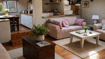 A spacious loft with a high ceiling, exposed wooden beams, a kitchen area, a seating area with a sofa and armchairs, and a dining table.