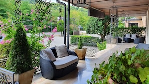 A covered outdoor seating area with a wicker sofa, potted plants, and a view of a lush green landscape. - HOTEL GIALLETTI (Orvieto)