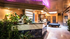 A hotel lobby with a marble reception desk, potted plants, a round seating area, and a modern ceiling design. - HOTEL GIALLETTI (Orvieto)