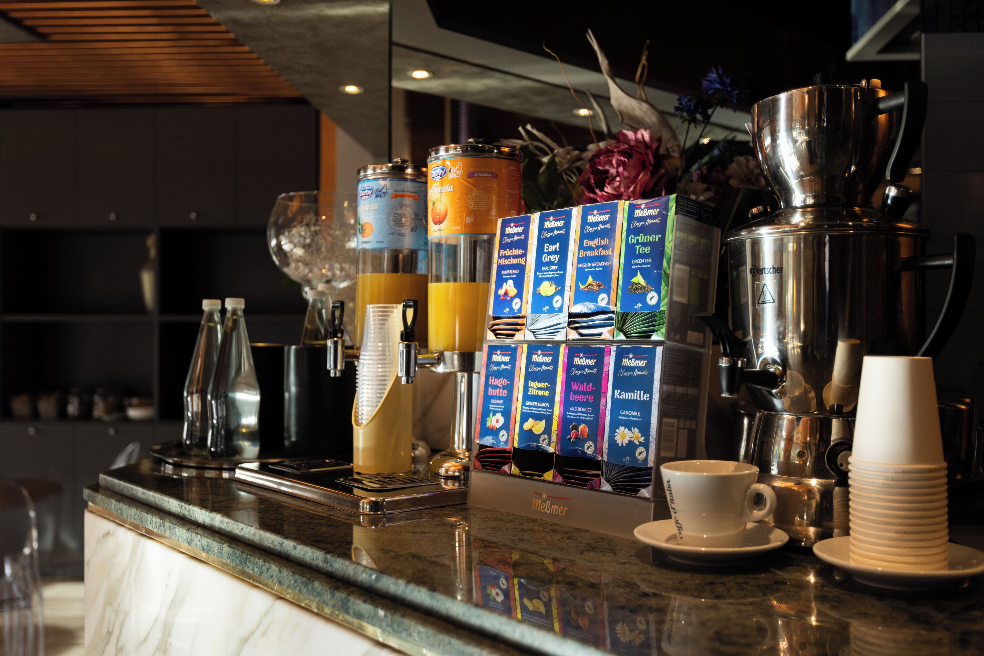 A coffee bar with various coffee machines, a stack of disposable cups, and a selection of coffee pods.