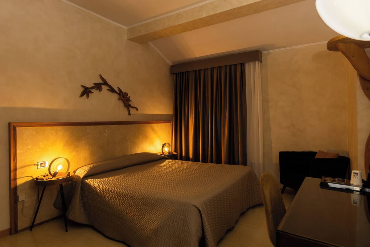 A hotel room with a large bed, bedside lamps, a small table, and a chair.