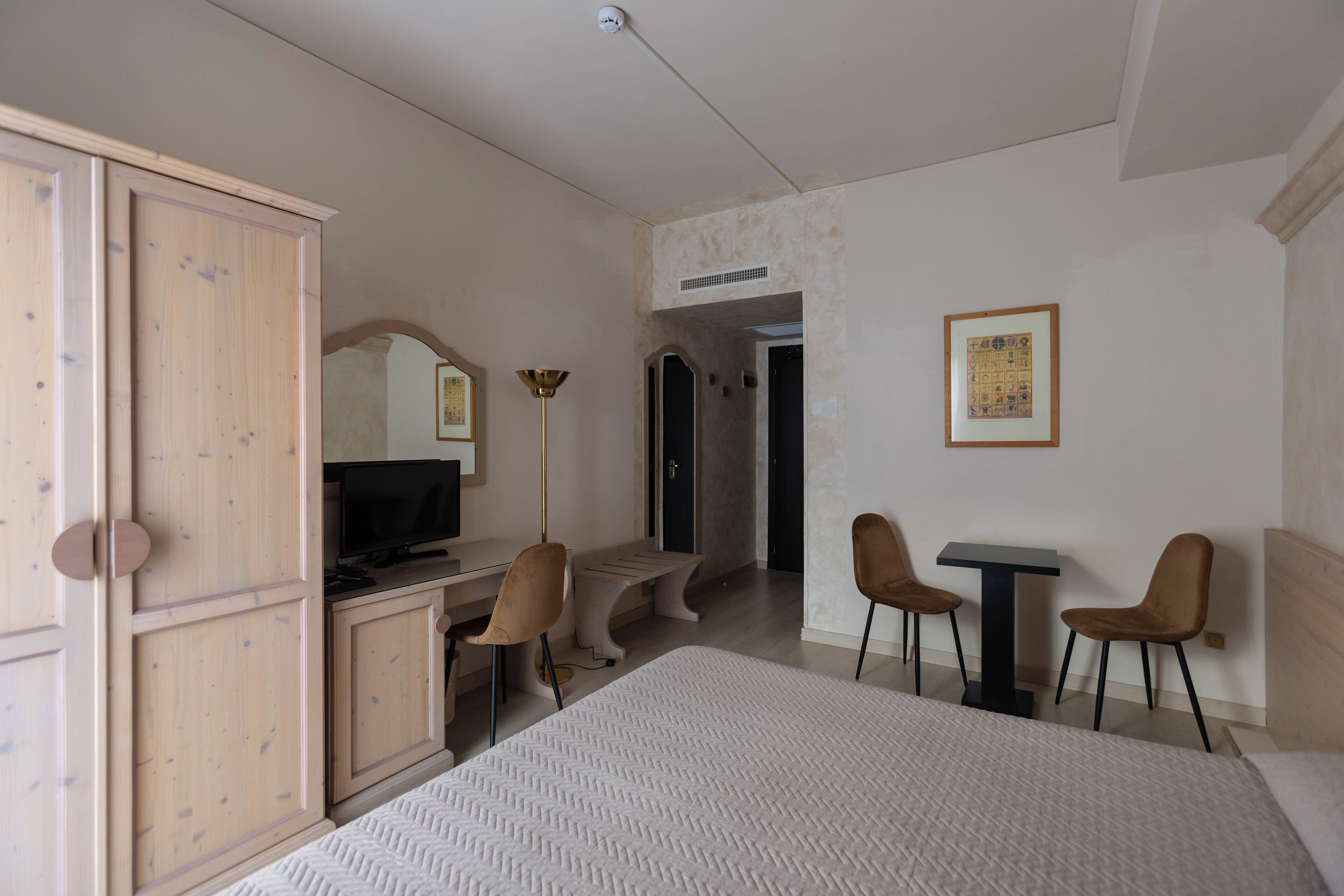 Una camera d'albergo con un letto, una scrivania con un computer, due sedie, una TV e un quadro appeso al muro.