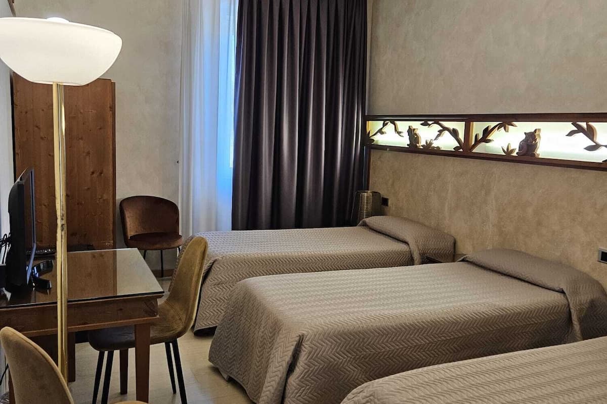 A hotel room with two beds, a desk, a chair, a lamp, and a window with curtains.