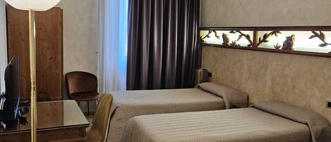 A hotel room with two beds, a desk, a chair, a lamp, and a window with curtains.