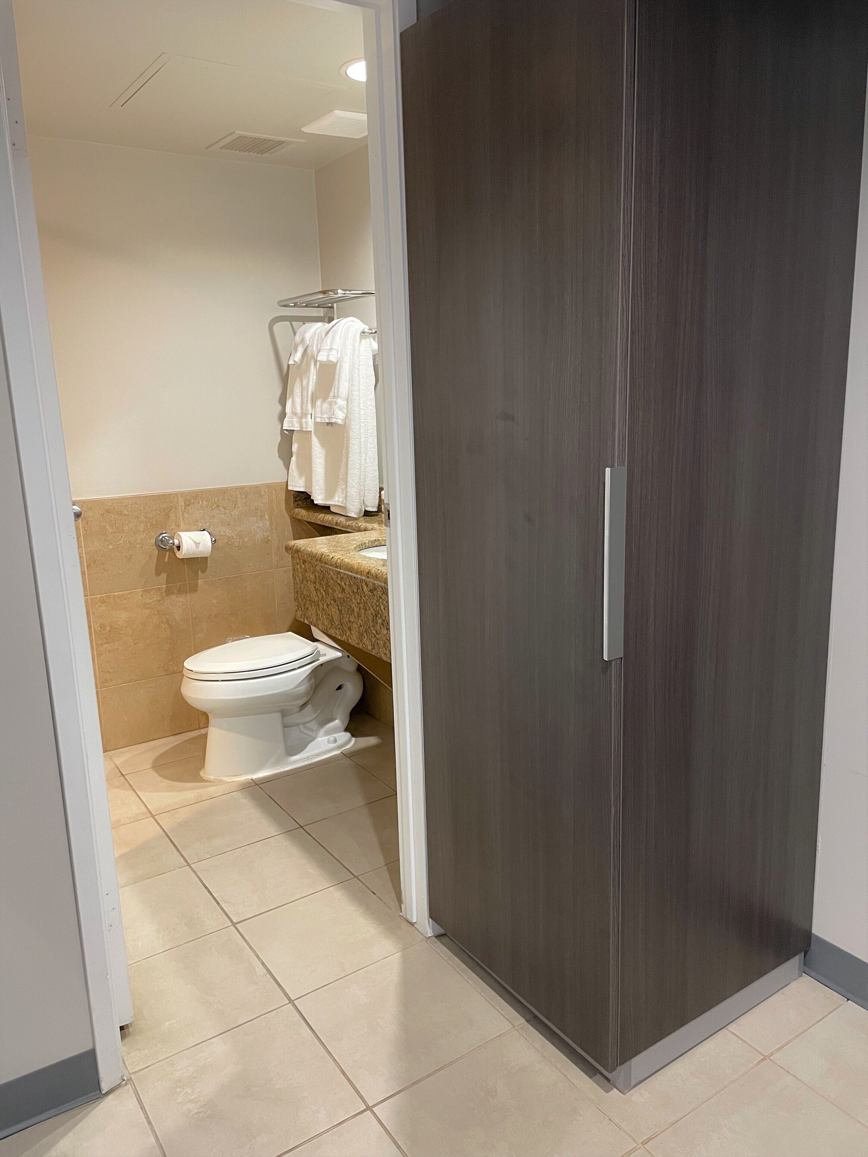 A bathroom with a toilet, a towel rack with towels, and a mirror.