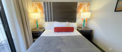 Een hotelkamer met een groot bed, twee nachtkastjes met lampen, een hoofdbord met een bladmotief en een raam met gordijnen.
