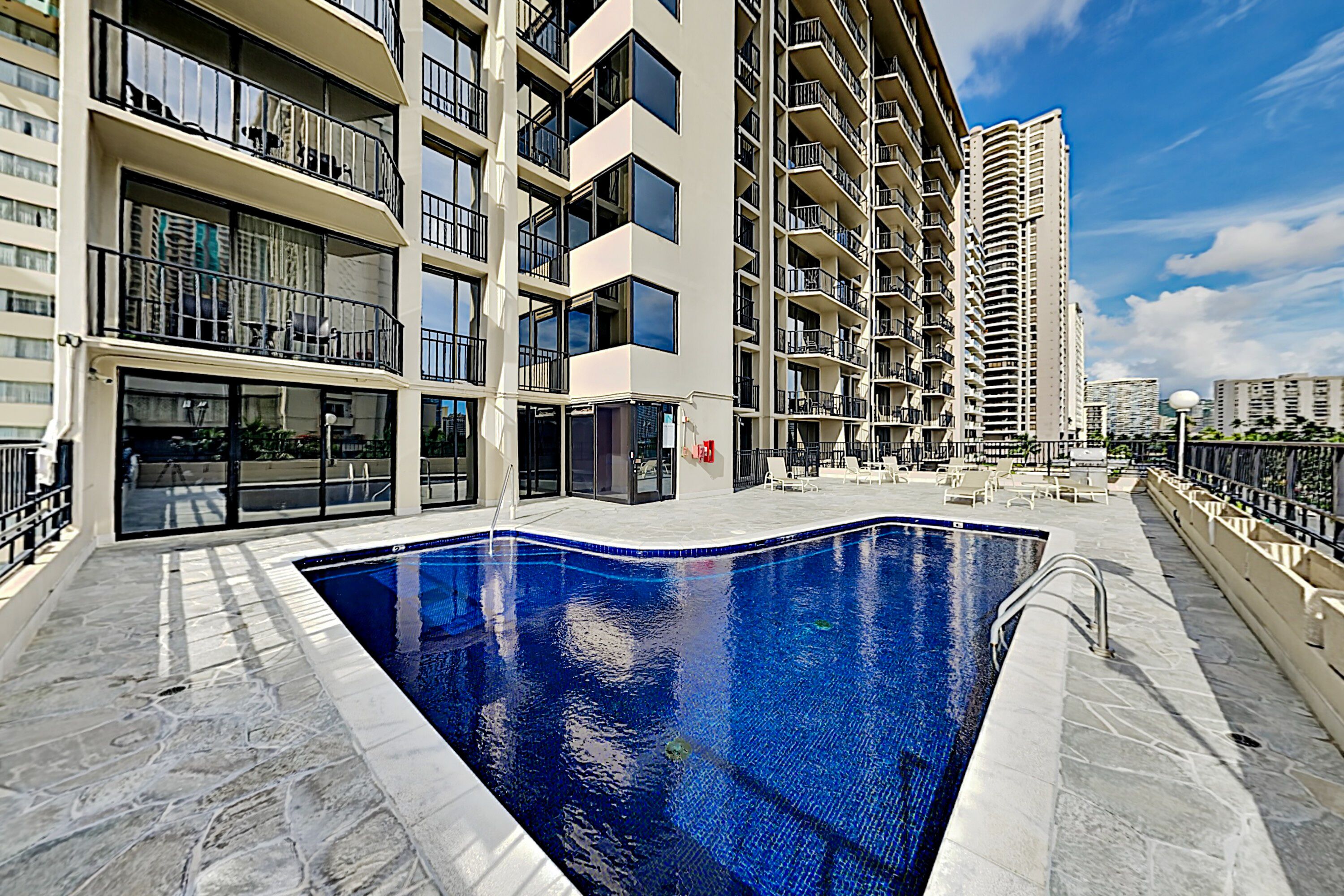 A modern apartment building with a swimming pool, balconies, and a clear sky.