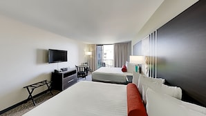 Une chambre d’hôtel avec deux lits, une télévision, un bureau et une fenêtre avec des rideaux.