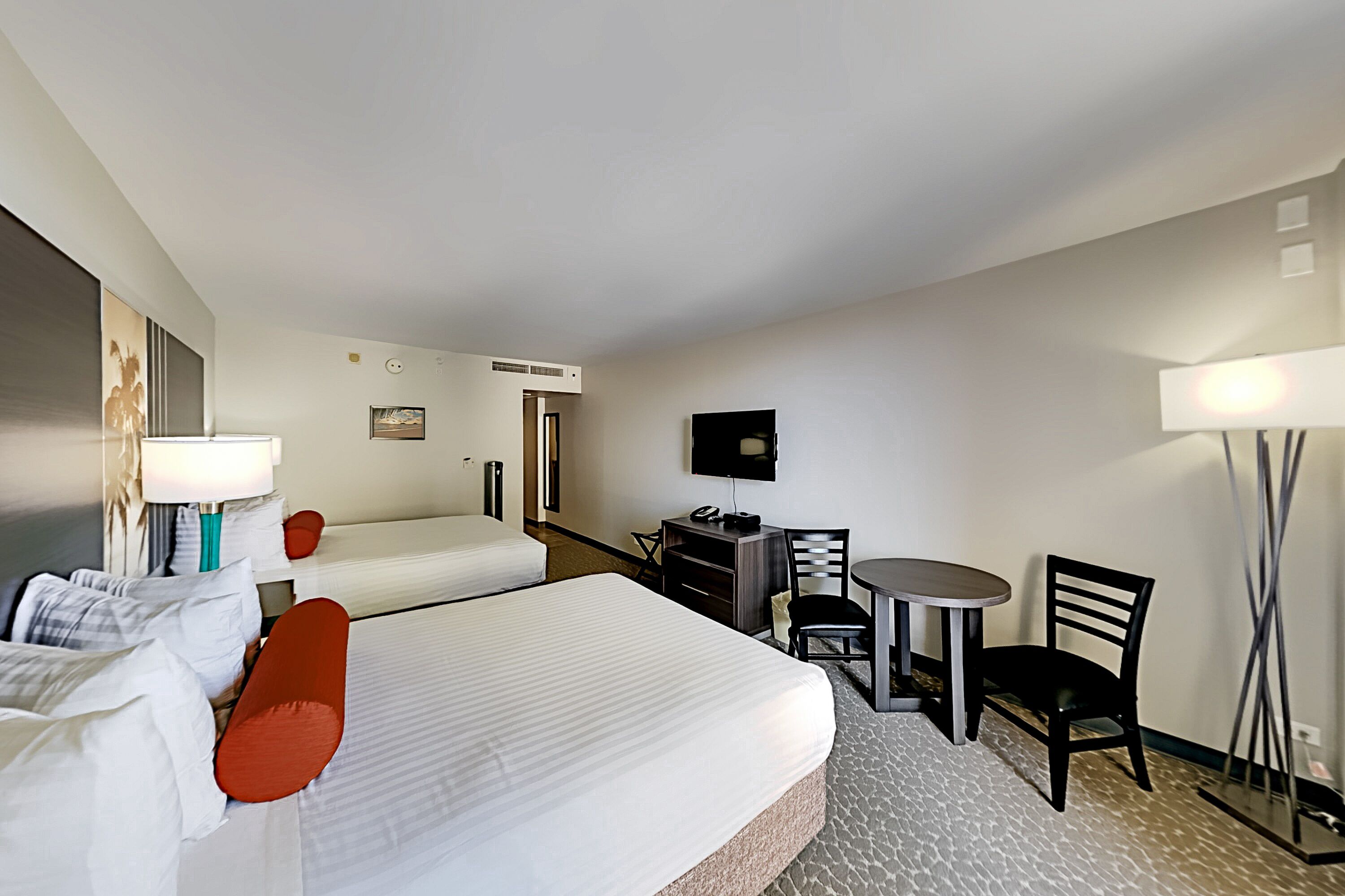 A hotel room with two beds, a desk with a chair, a TV, and a lamp.