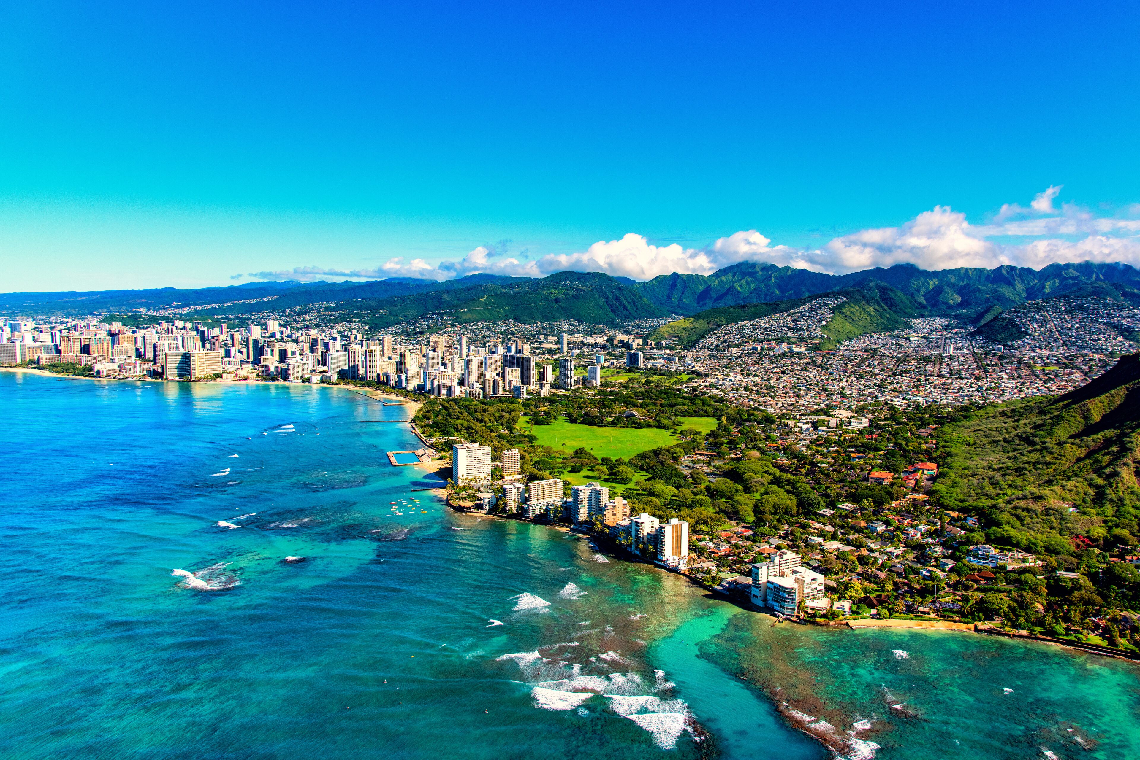 A coastal cityscape with a dense urban area, a beach, and mountainous terrain in the background.