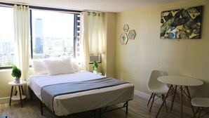 Camera d'albergo con un letto, un tavolino, due sedie, una finestra con tende e vista sulla città.