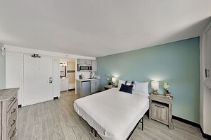 Une chambre d’hôtel comprenant un lit, des tables de chevet, une commode, un bureau, une kitchenette et une salle de bain.