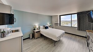 Ein Hotelzimmer mit Bett, Nachttischen, einer kleinen Küchenzeile, einem Fernseher und einem großen Fenster mit Blick.