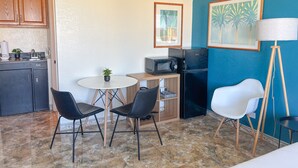 A compact kitchen with a sink, microwave, and refrigerator, a small dining table with two chairs, and a single potted plant. - Updated! Humble Hawaiian Monarch Studio | Pool (Honolulu)