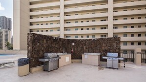 An outdoor pool area with a stone wall and two barbecue grills. - Mellow Hawaiian Monarch Studio | Pool + Gym (Honolulu)