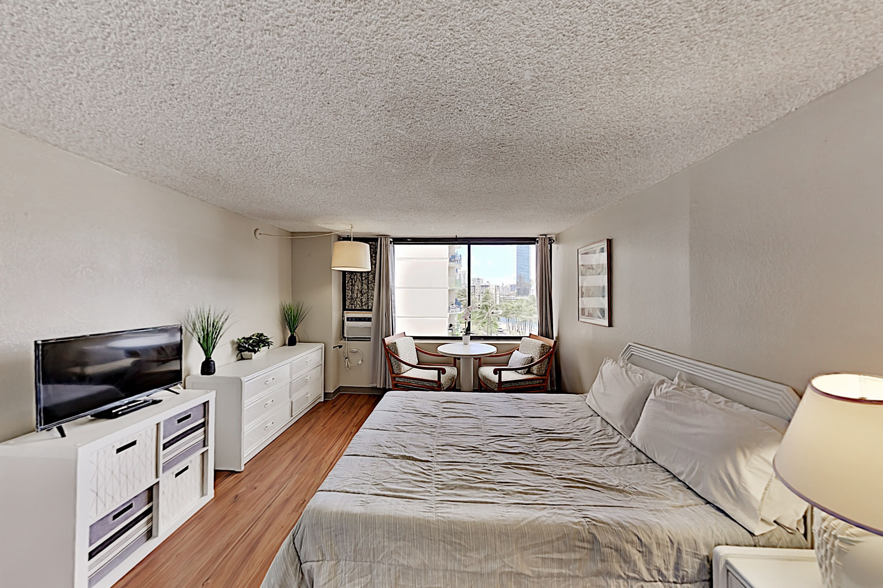 A hotel room with a bed, a TV, a desk, a chair, a table, and a window with a city view.