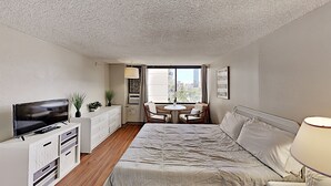 Habitación de hotel con cama, televisión, escritorio, silla, mesa y ventana con vista a la ciudad.