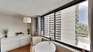 Una habitación de hotel moderna con un ventanal grande, una mesa redonda, un tocador blanco y dos plantas en macetas.