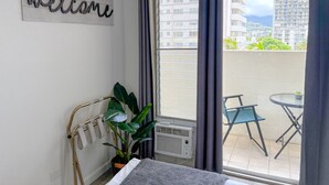 A balcony with a view of buildings, a welcome sign, a potted plant, and a small table with a chair. - Refreshed! Breezy Kuhio Village Studio | Lanai (Honolulu)