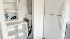 A kitchen with a white refrigerator, a built-in ironing station, and a broom leaning against the wall. - Refreshed! Breezy Kuhio Village Studio | Lanai (Honolulu)