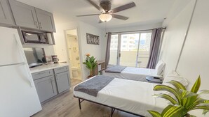 Ein kompaktes Hotelzimmer mit Küchenzeile, zwei Betten, Deckenventilator und Balkon mit Aussicht.