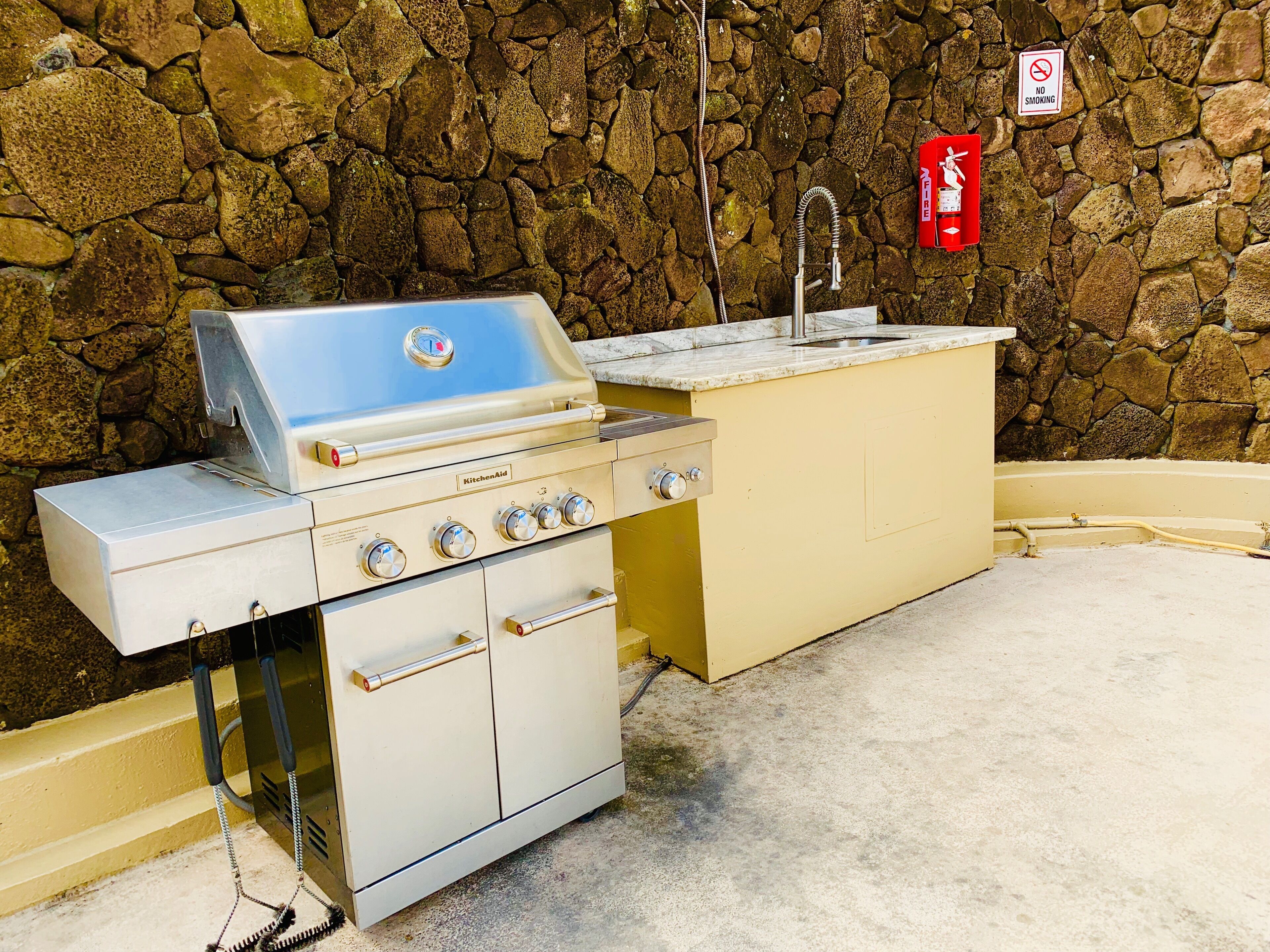An outdoor kitchen with a stone wall backdrop, a built-in sink, and a fire extinguisher.