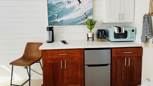 A kitchen with a coffee maker, toaster, and microwave on the counter, a potted plant, and a framed picture of surfers on the wall. - Modern Surf Chic Studio at Hawaiian Monarch | Pool (Honolulu)