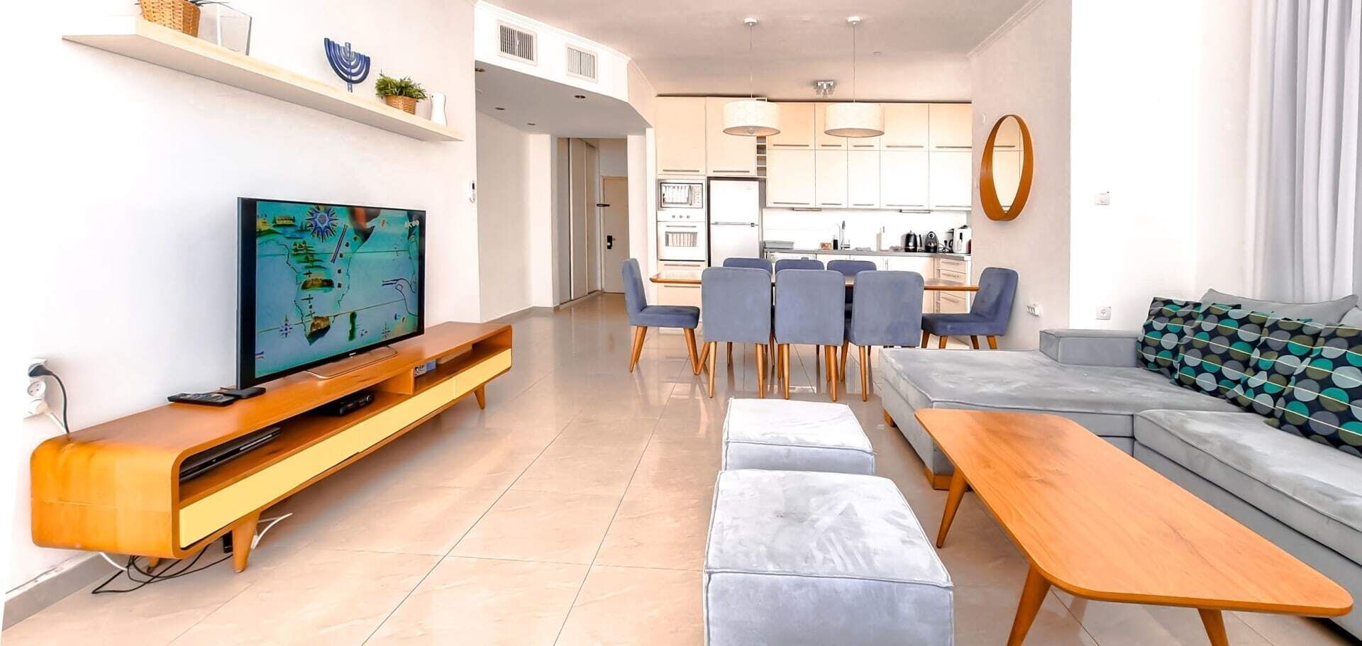 Una sala de estar moderna con un televisor de pantalla plana, un sofá, un comedor con sillas y una cocina al fondo.