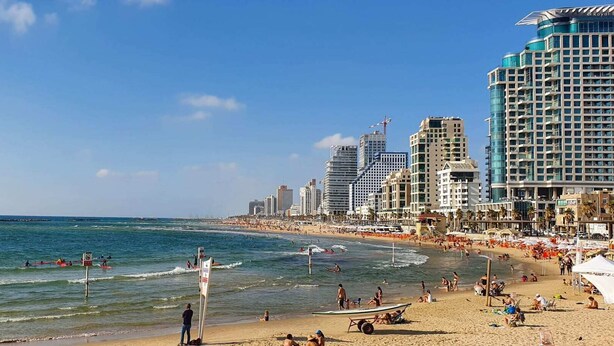 A beach with a cityscape in the background, including high-rise buildings and a clear sky.
