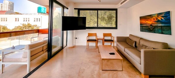 Ein modernes Wohnzimmer mit einer Couch, zwei Sesseln, einem Couchtisch und einem Fernseher an der Wand.
