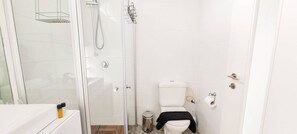 Ein Badezimmer mit Glasdusche, Toilette und Waschbecken mit Ablagefläche.