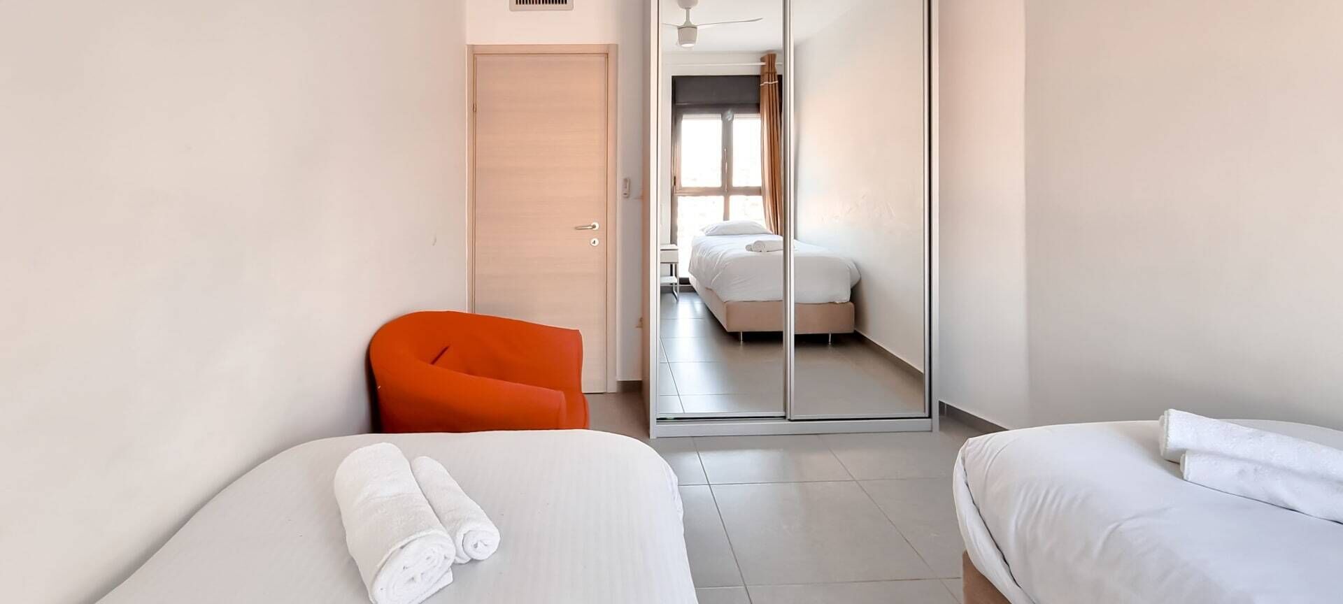 A hotel room with two beds, a sliding door leading to a bathroom, and an orange chair.