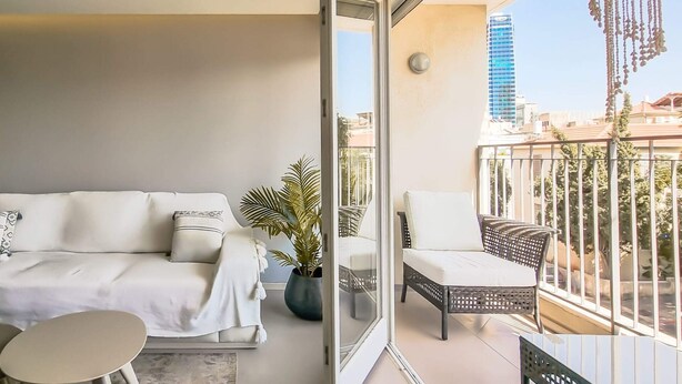 A balcony with a white sofa, a small table, and a potted plant. - Pines Belle - Two Bedroom Apartment, Sleeps 4 (Tel Aviv-Yafo)