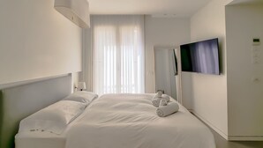 A hotel room with a large bed, a TV mounted on the wall, and a door to the right. - Pines Belle - Two Bedroom Apartment, Sleeps 4 (Tel Aviv-Yafo)