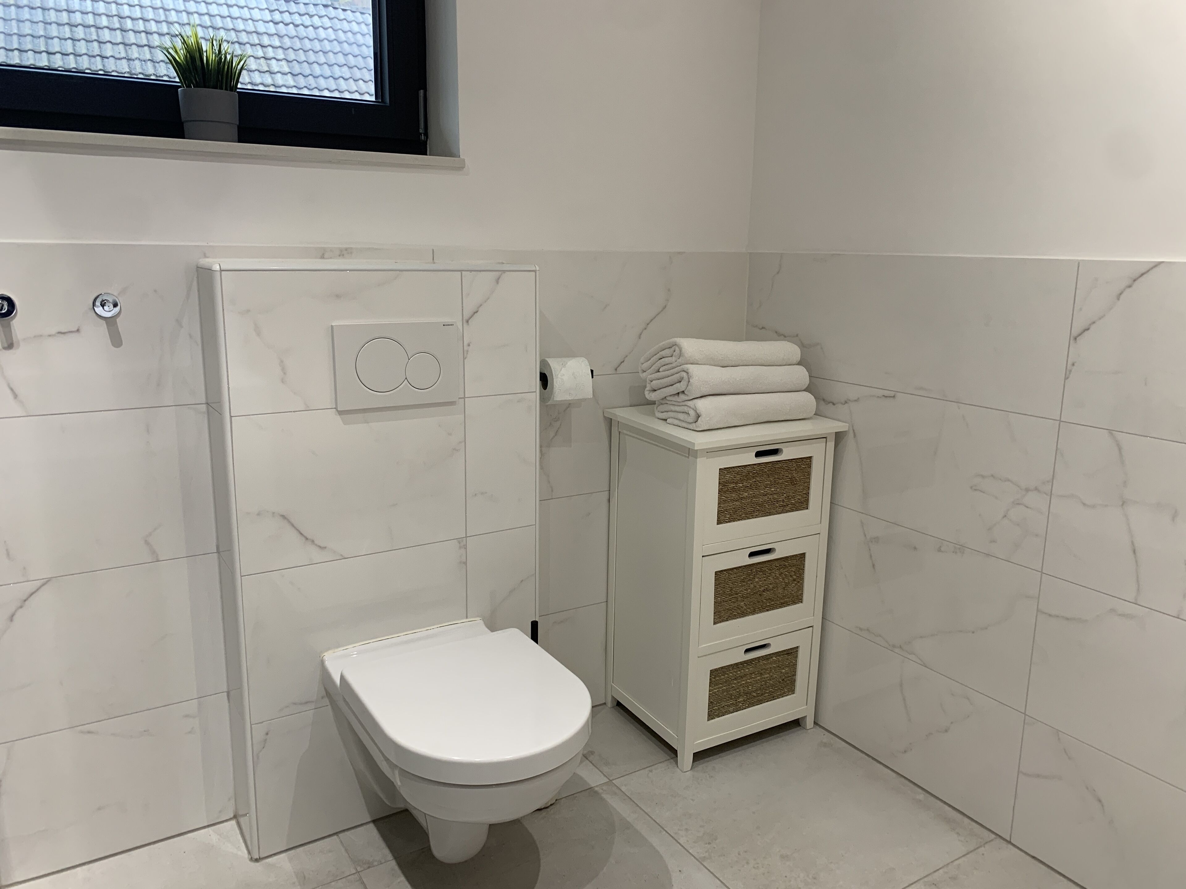 A modern bathroom with a toilet, a towel rack, and a small cabinet.