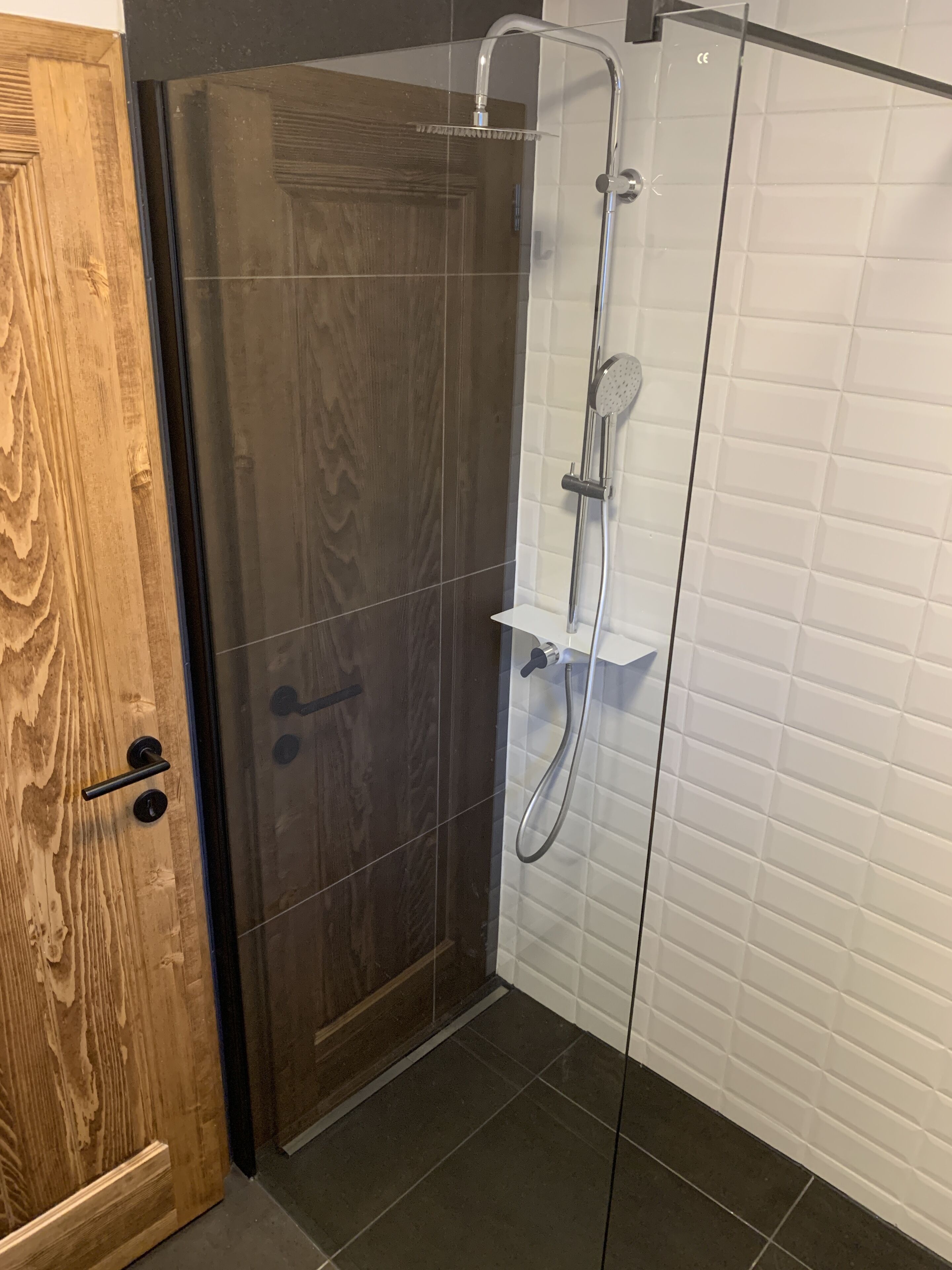 Une douche fermée par des parois en verre, dotée d’un pommeau de douche à main et d’un robinet fixé au mur.