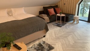 A modern bedroom with a large bed, a sofa, a small round table, and a potted plant. - Pine Tree Holiday House (Kranjska Gora)