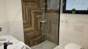 Une salle de bain moderne avec une douche à parois de verre, un lavabo blanc avec un robinet noir, des toilettes et une fenêtre donnant sur un toit recouvert de tuiles.