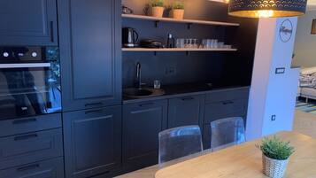 Una cocina moderna con armarios oscuros, horno empotrado, un lavabo y una zona de comedor con una mesa y sillas de madera.