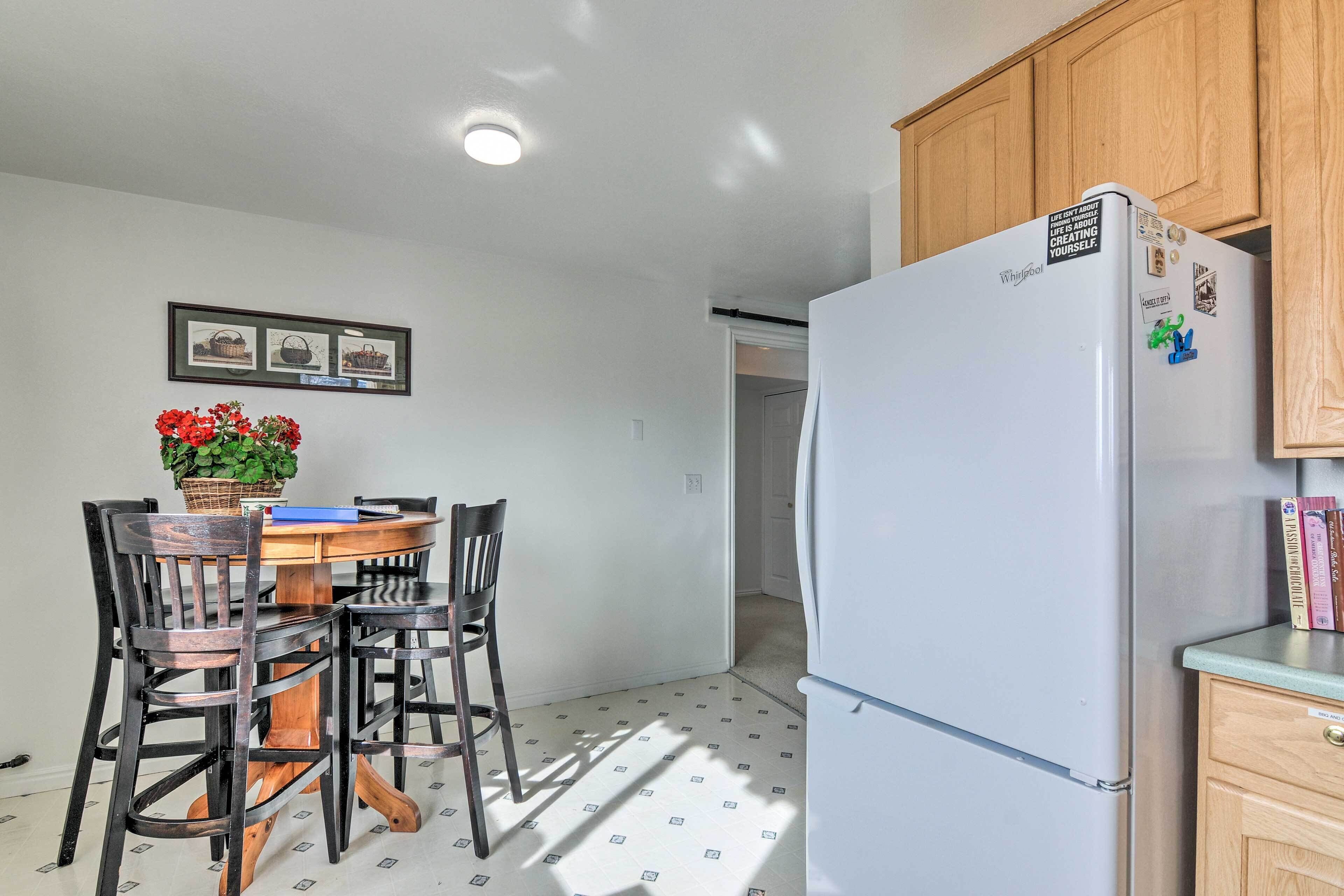 Una cocina con refrigerador, armarios de madera, una mesa de comedor con sillas y una planta en maceta.